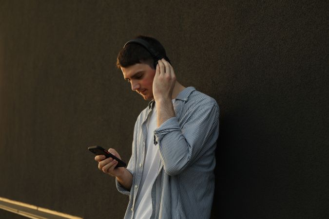 Young man in headphones listen music against wall