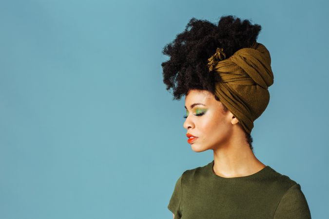Studio shoot of Black woman with her eyes closed wearing a green hair scarf