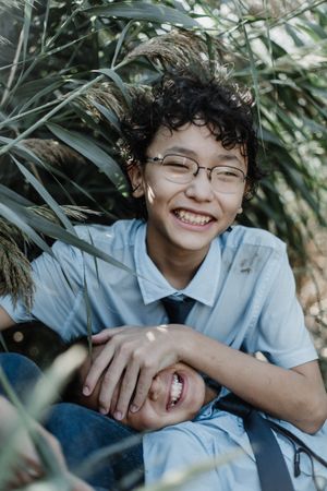 Smiling boy in curly hair with younger brother by bush