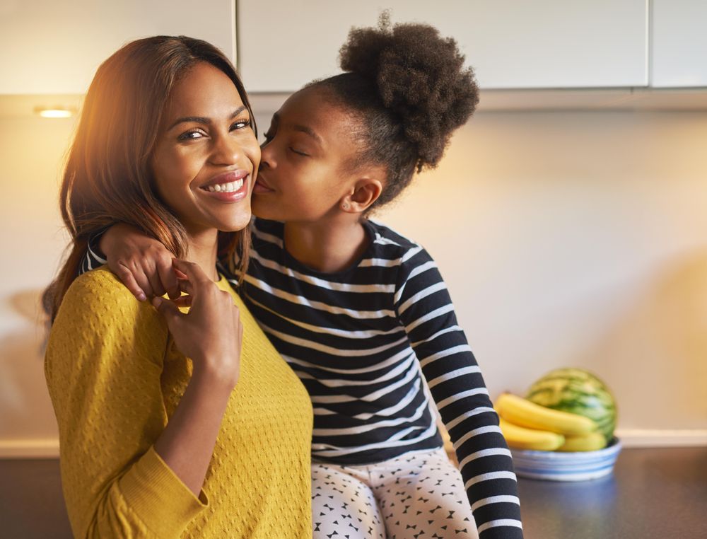 Daughter kisses smiling mother in a sunny kitchen