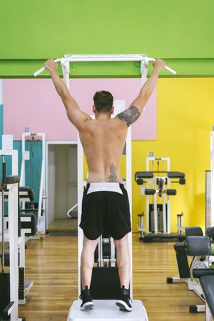 Back of man working out in a fitness club on pull up bar