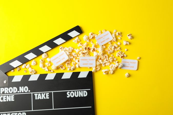 Flat lay composition with clapperboard, popcorn and tickets on yellow background