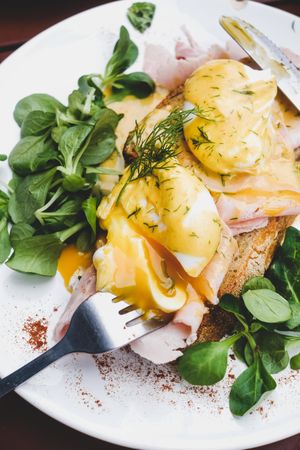 Eggs Benedict with yoke broken with greens, coffee, top view, close up