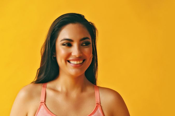 Headshot of smiling Hispanic woman looking to her side in a yellow room
