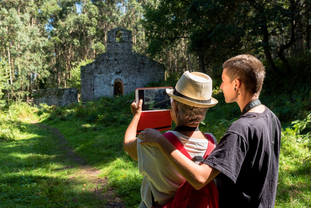 Woman hugging mature woman while taking picture on tablet in forest