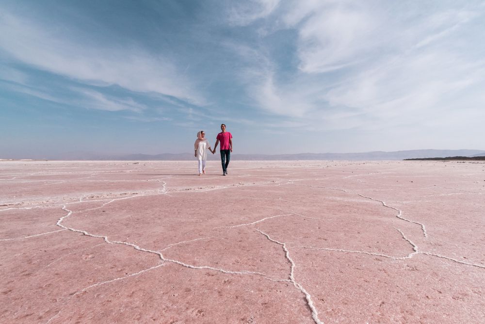 Happy relaxed travelers enjoying unusual scenery of pink salt lake in sunny day