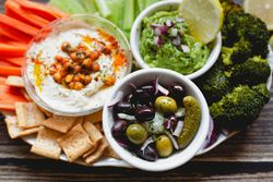 Tasty hummus and sauces decorated with bright cut vegetables on table
