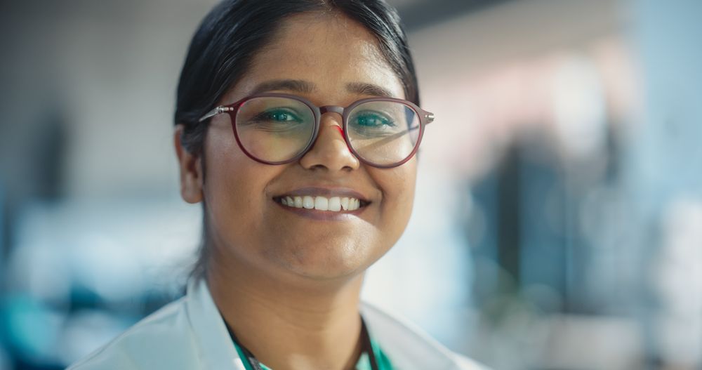 Portrait Close Up of Indian Female Specialist Wearing Lab Coat and Glasses Smiling.
