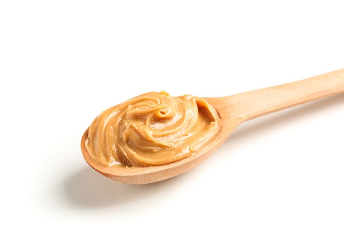 Creamy peanut butter in wooden spoon isolated on light background, closeup. A traditional product of American cuisine