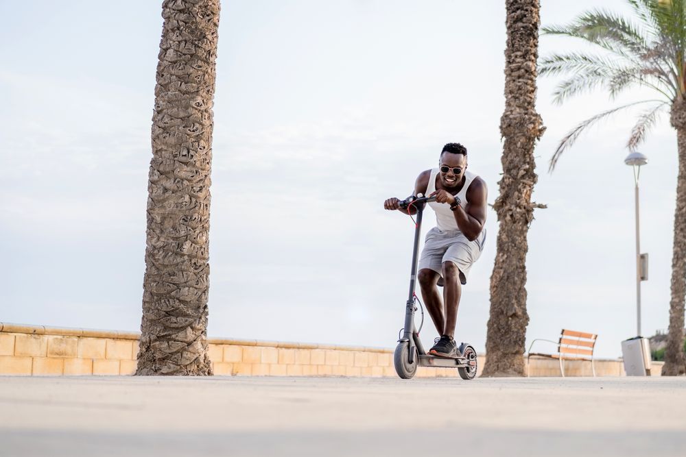 Cool adult Black man riding scooter in street