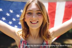 Close up of a smiling girl holding American flag behind her bYVKG0