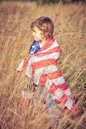 Adorable preteen boy rolled in American national flag in field