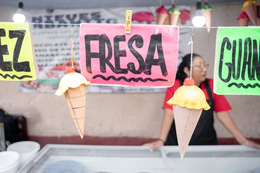 Nut and strawberry flavor signs in an ice cream street market stall with an Hispanic woman in the background