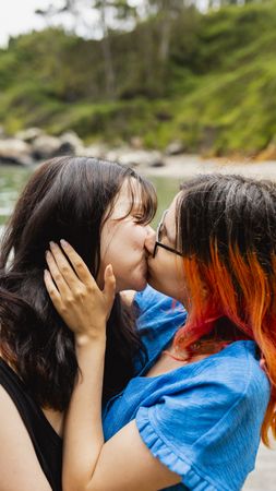 Two young lesbian women kiss passionately, on a natural beach in summer