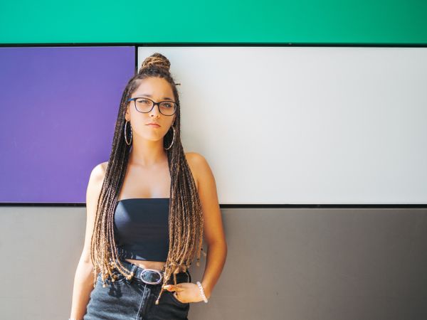 Charming teenage girl with braids in sunglasses nearby colorful wall