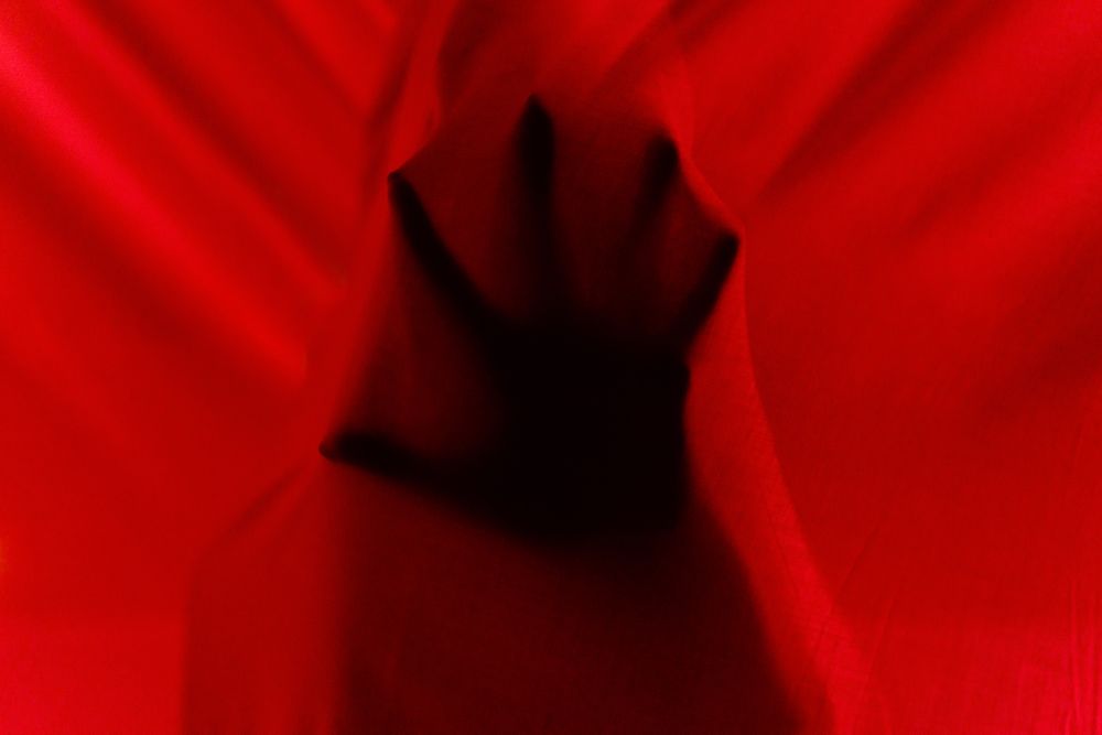 Faceless person hiding behind curtains at night time