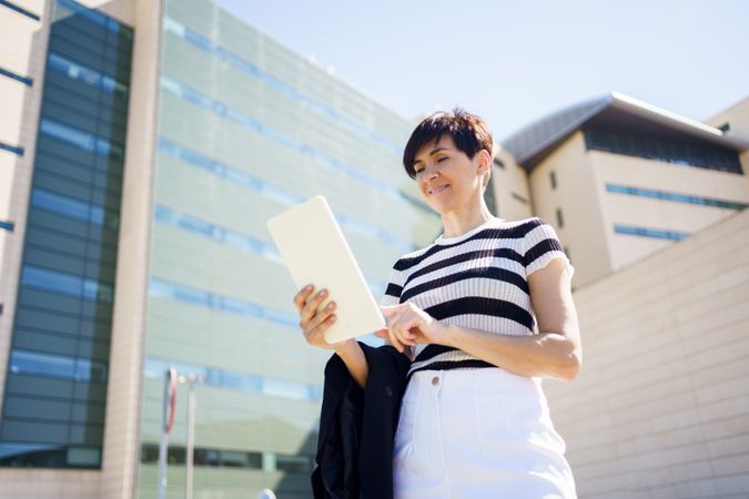 Woman standing outside building checking digital tablet 
