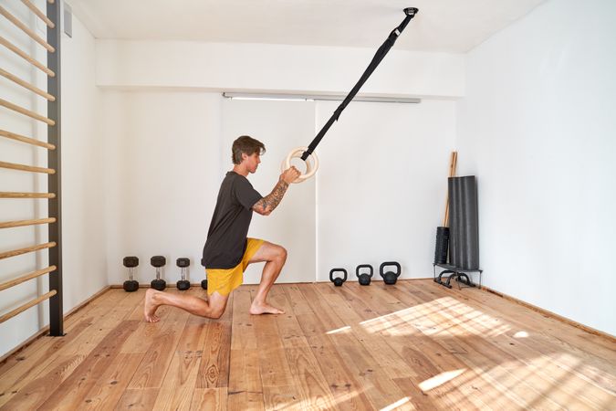 Serious sportsman hanging on gymnastic rings and kneeling