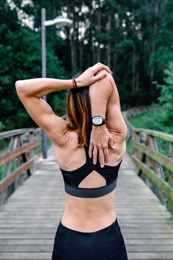 Unrecognizable sportswoman doing stretching arms outdoors