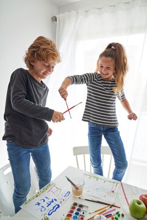 Happy children playing with paintbrushes near white table