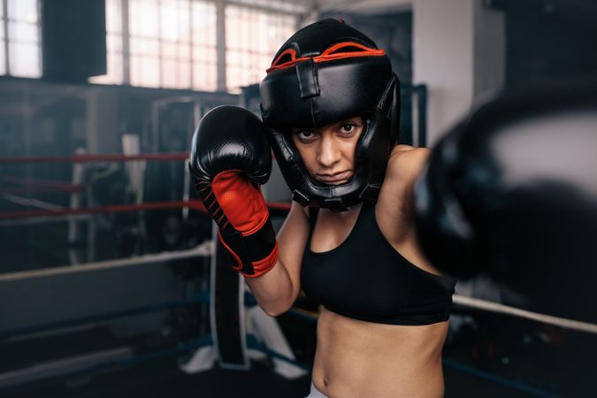 Portrait of female boxer in head gear & gloves training in the ring