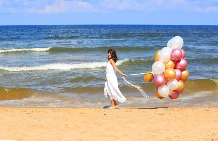 Woman in light dress holding balloons on beach