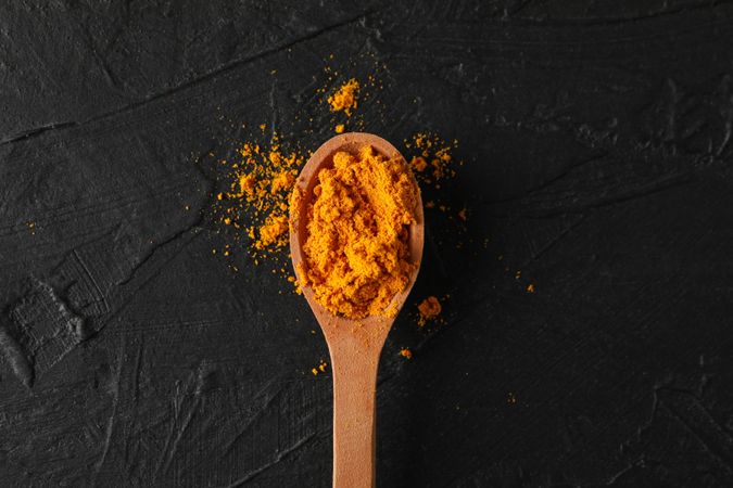 Looking down at wooden spoon of colorful turmeric