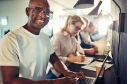 Man smiling while working on his laptop in an open office