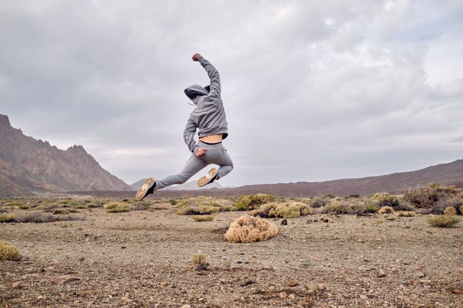 Carefree man traveler jumping on rocky ground near hills