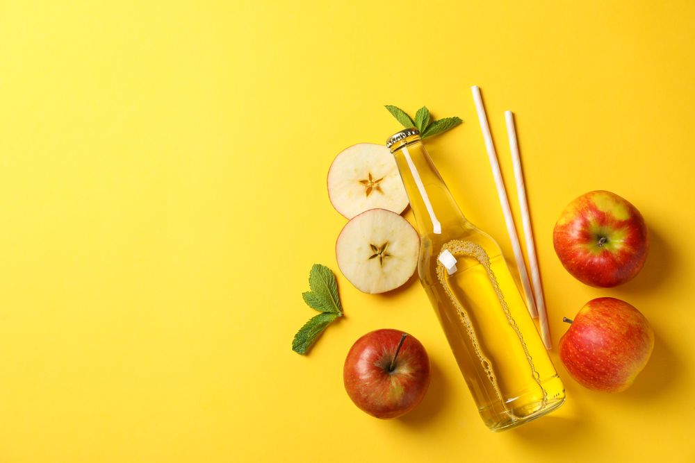 Composition with cider, apples and straws on yellow background