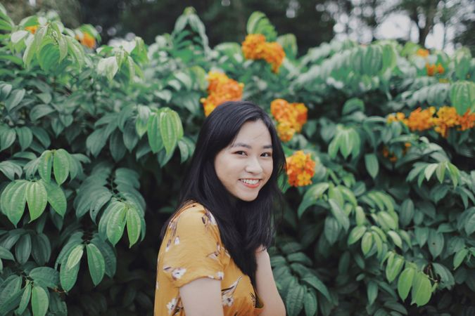 Woman in yellow floral dress standing beside tree