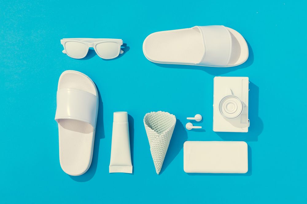 Summer objects of flip flops, sunglasses, camera, smart phone, EarPods on blue background