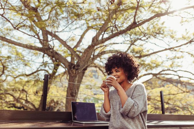 Curly haired woman sitting outdoors with coffee cup in her hands