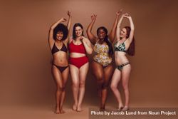 Full length of slim and curvy women in bikinis dancing together over brown background 4dYjlb