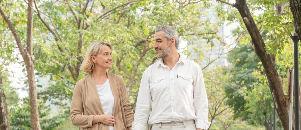 Mature man and woman walking hand in hand in park, banner