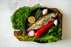 Top view of trout fish ready for cooking with lemon, onion and pepper