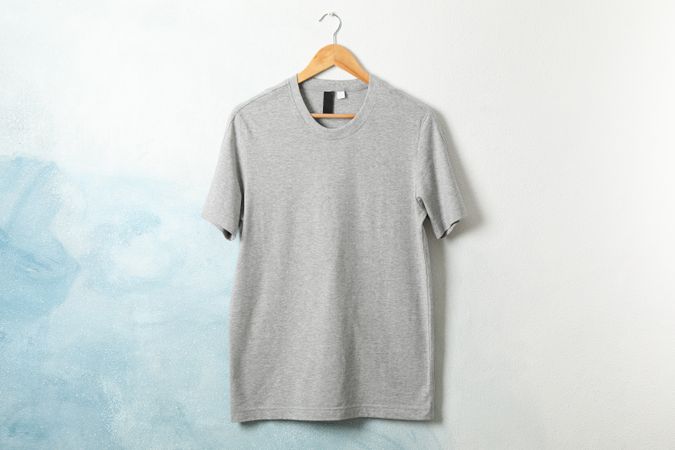 Hanger with blank gray t-shirt on blue background, space for text