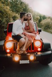Loving couple sitting on car on road near forest