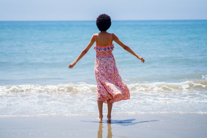 Rear shot of woman with outstretched arms facing blue ocean
