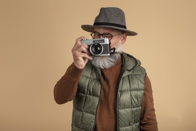 Middle aged man with a hat holding a camera standing against yellow background