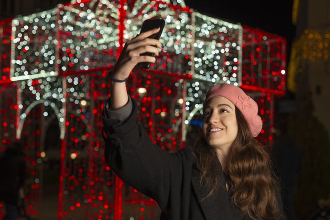 Happy young woman in cap standing and taking selfie with smartphone