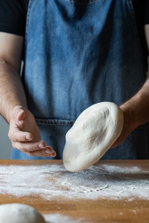 Crop man flattening dough for pizza