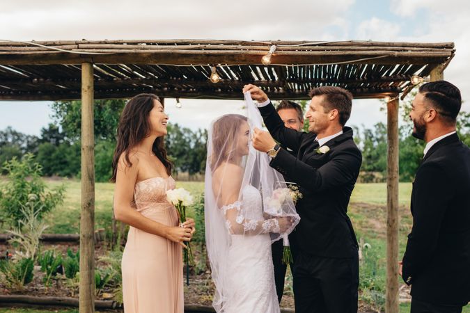 Handsome groom lifting up bridal veil to kiss beautiful bride