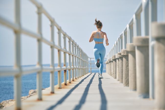 Unrecognizable jogger running on bridge above ocean during worko