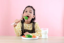 Asian Girl Eating Healthy Vegetables and Drinking Milk
