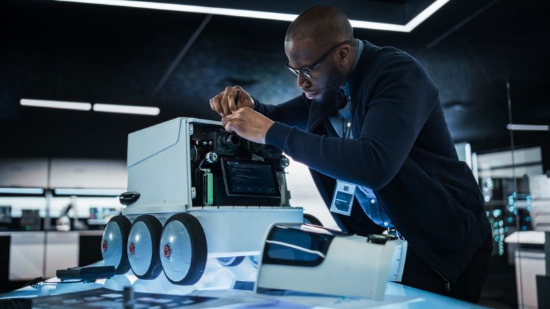 Portrait of an Engineer Using a Screwdriver While Developing a Remotely Controlled Delivery Robot. Black Specialist Working in High Tech Research Laboratory with Modern Equipment
