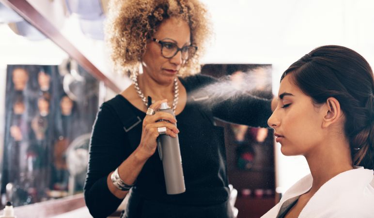 Mature hairstylist spraying client’s hair with hairspray