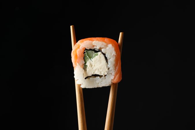 Chopsticks with sushi roll on dark background, close up. Japanese food