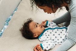 Smiling baby boy lying down with his mother making faces at him