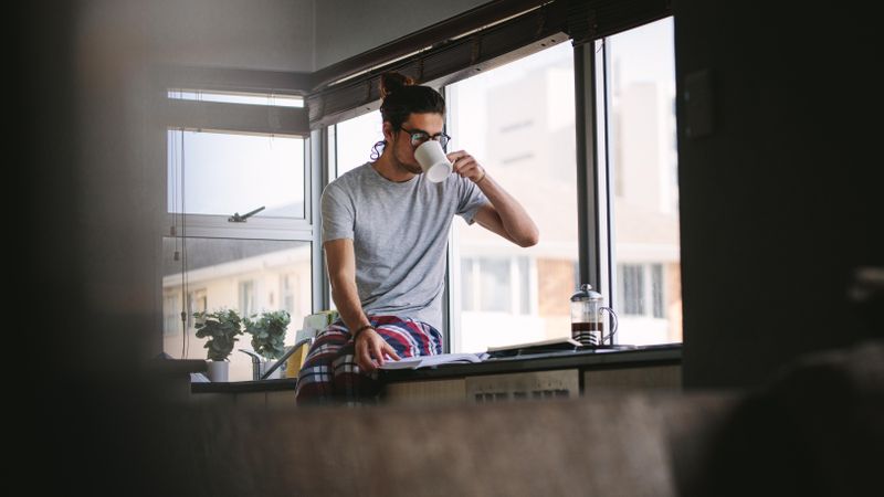 Young male sitting on kitchen counter drinking coffee in the morning